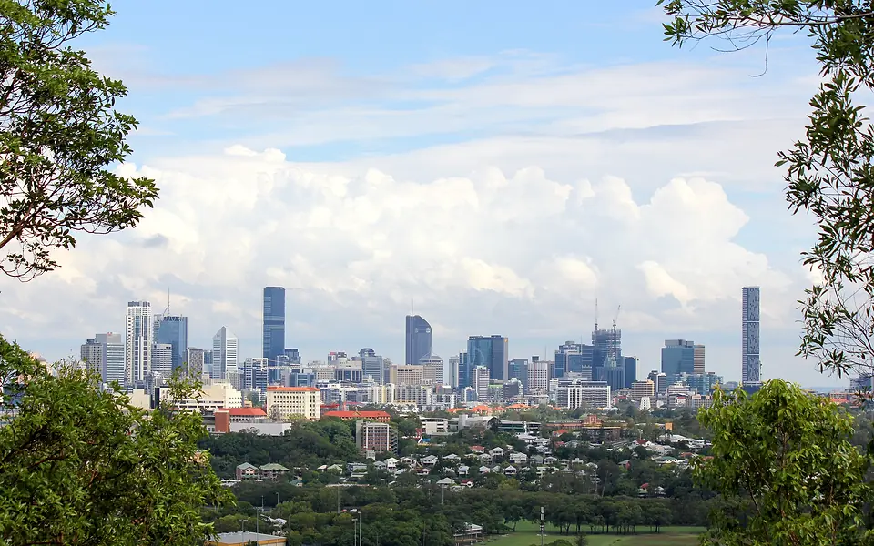City skyline of office towers seen across leafy suburbs and framed by overhanging tree branches