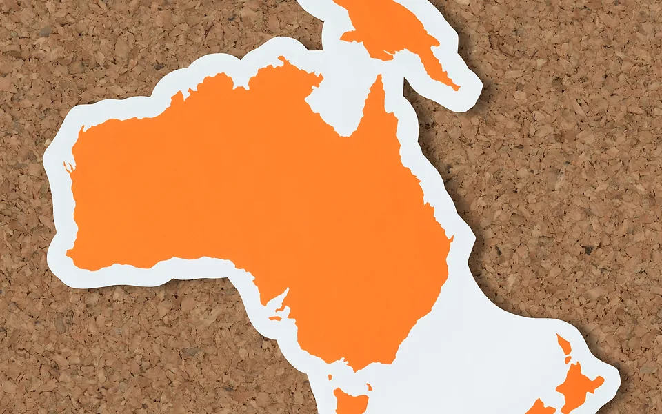 Orange paper cut-out map of Australia with a white border on a cork board, cropped at top and bottom