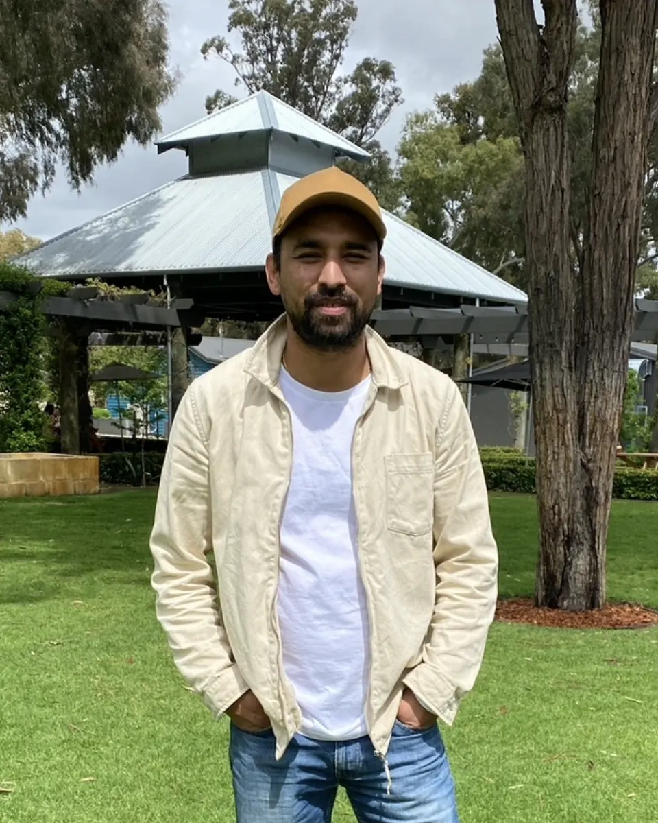 Ron Shrestha, director of Ads Camps, smiling outdoors in a tan cap and cream overshirt