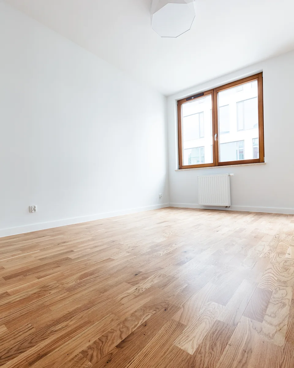 Empty room with freshly painted white walls, a timber-framed window and polished timber floorboards
