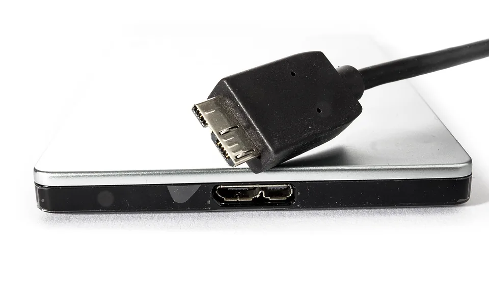 Black USB cable plug resting on a slim silver external hard drive, on a white background