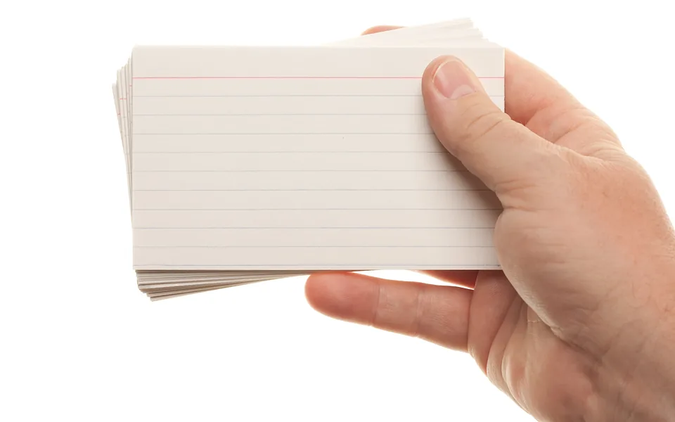 Hand holding a thick stack of blank ruled index cards against a white background