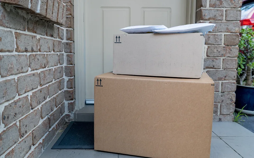 Two cardboard parcels stacked on the doorstep of a brick house in front of a white front door