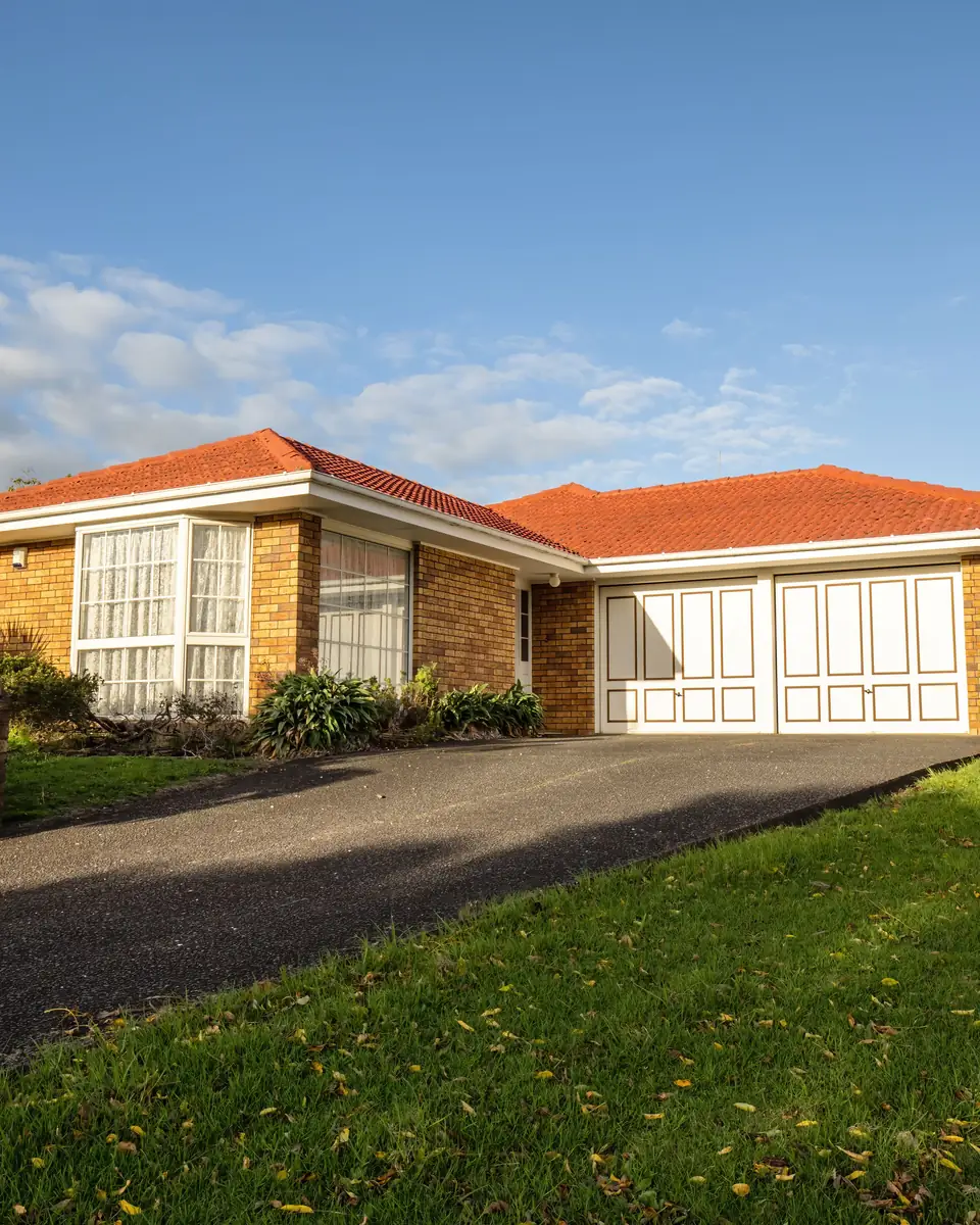 Single-storey brick house with a terracotta tiled roof, double garage, driveway and sloping front lawn