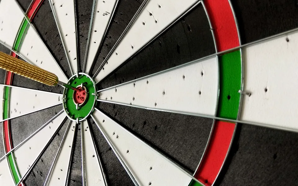 Brass dart lodged in the red bullseye of a dartboard, shown in close-up from the side