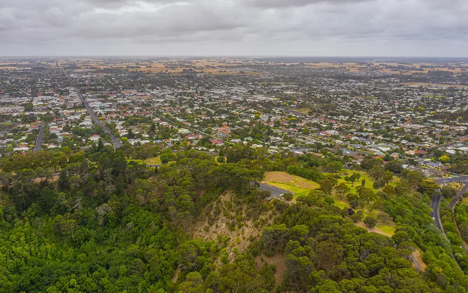 Aerial view over a wooded hilltop park to the streets and rooftops of a regional town under cloud