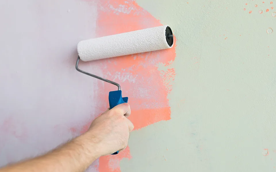 Painter's hand rolling pale green paint over a pink wall, with the old and new colours side by side