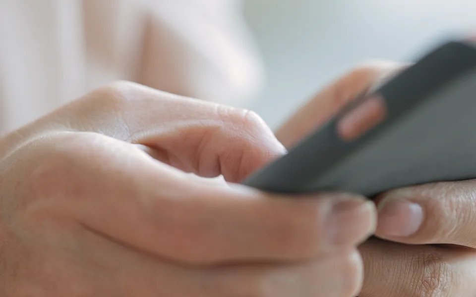 Extreme close-up of two hands holding a dark smartphone, with a thumb resting on the screen
