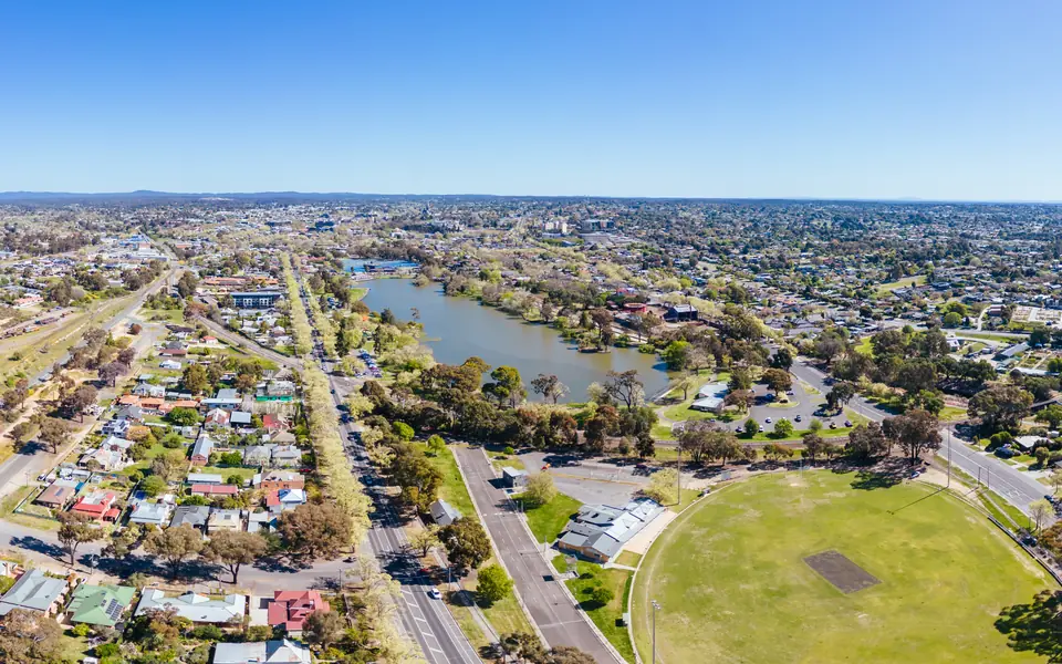 Aerial view of a regional town with a lake, a tree-lined main road and a green sports oval