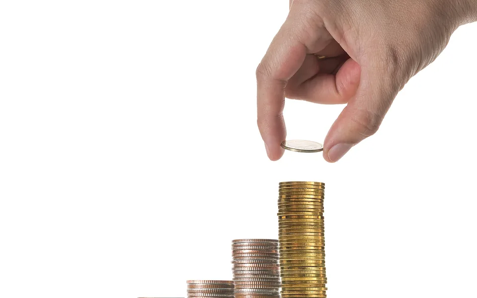 Hand placing a coin on the tallest of three rising stacks of coins against a white background