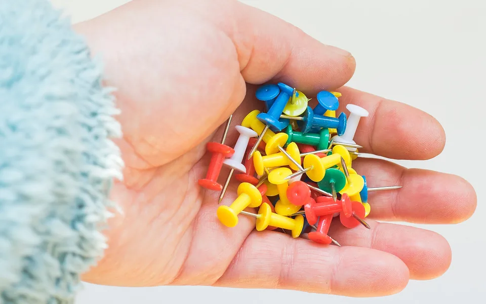 Open palm holding a handful of plastic push pins in red, yellow, blue, green and white