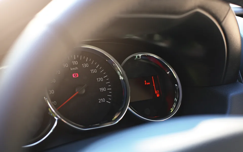 Close-up of a car's speedometer and instrument dials seen past the edge of the steering wheel