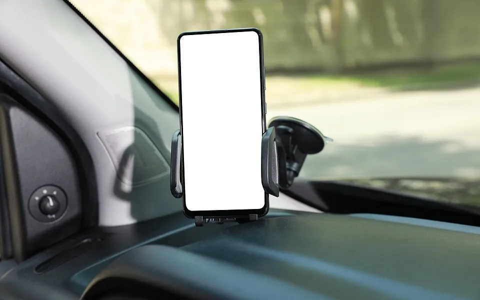 Smartphone with a blank white screen held in a car dashboard mount, with a sunlit street outside