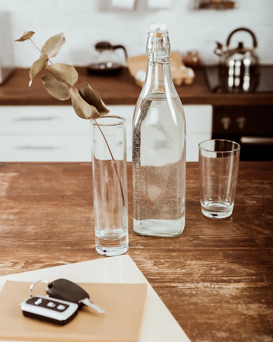 Glass water bottle, drinking glasses and a car key fob on a rustic timber kitchen table
