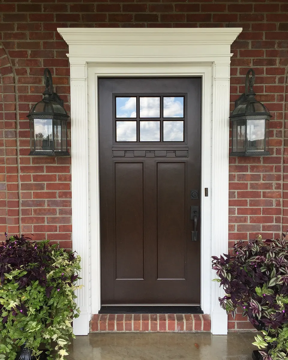 Dark timber front door with six small glass panes, set in a red brick wall between two lanterns