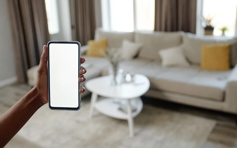 Hand holding a phone with a blank white screen in a lounge room with a cream sofa and round coffee table