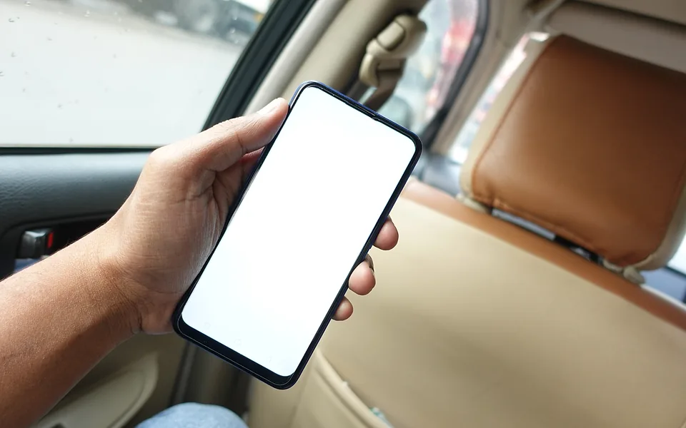 Hand holding a smartphone with a blank white screen inside a car with tan leather seats