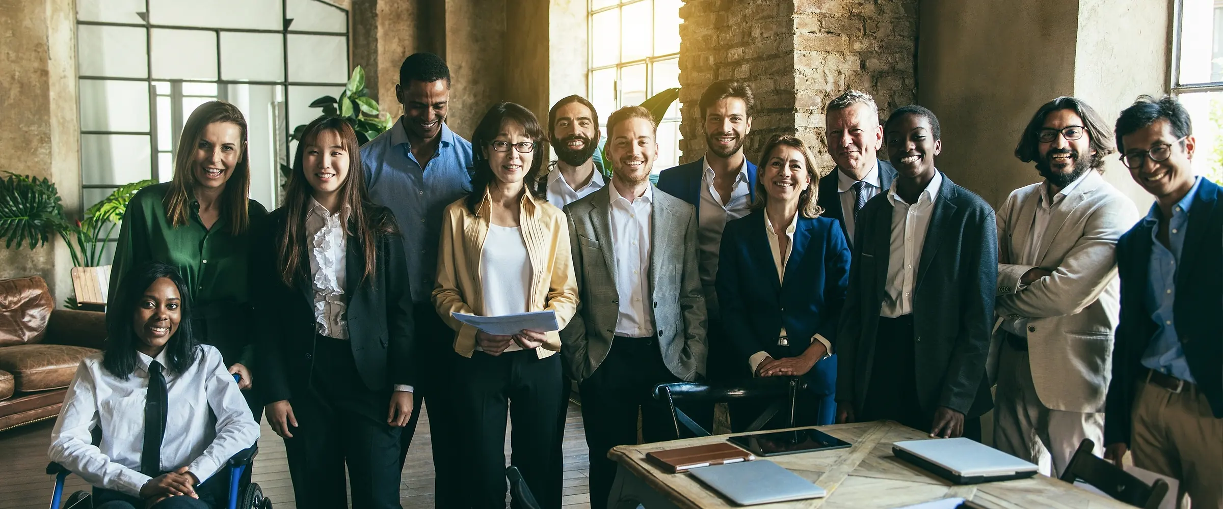 Group of smiling business people standing in a loft-style office beside a wooden meeting table (stock photo)