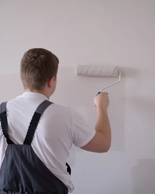 House painter facing away from the camera, running a paint roller up a freshly coated white wall