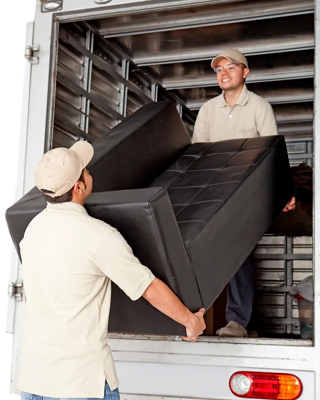 Removalist tradies in matching beige uniforms and caps carrying a leather couch out of their truck