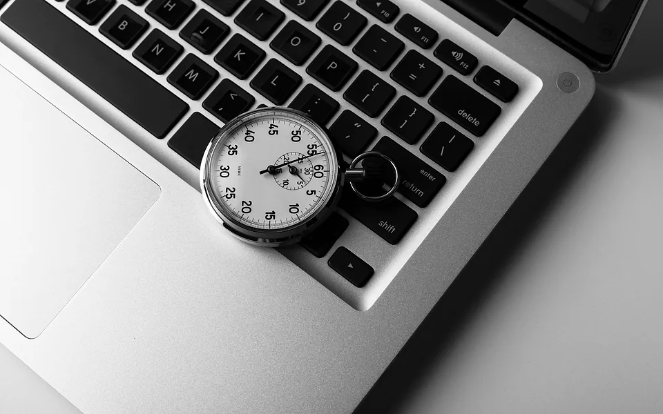 Black and white close-up of an analogue stopwatch resting on the keyboard of an open laptop