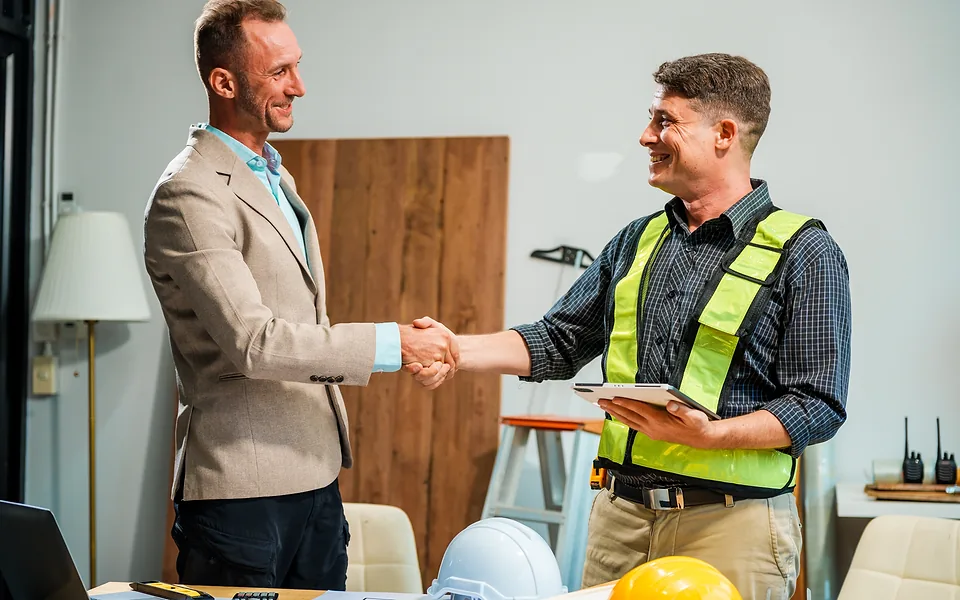 Man in a blazer shaking hands with a smiling tradie in a hi-vis vest who is holding a tablet